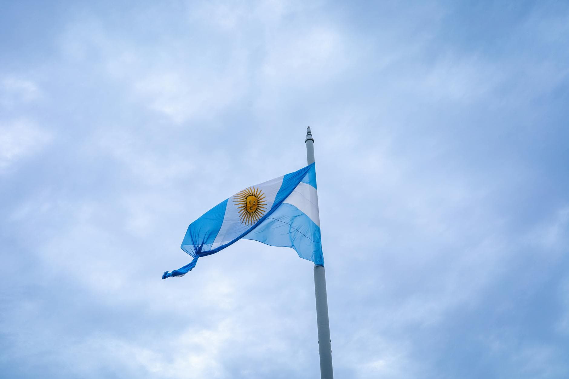 Bandera argentina ondeando al viento con un tranquilo cielo nublado de fondo.