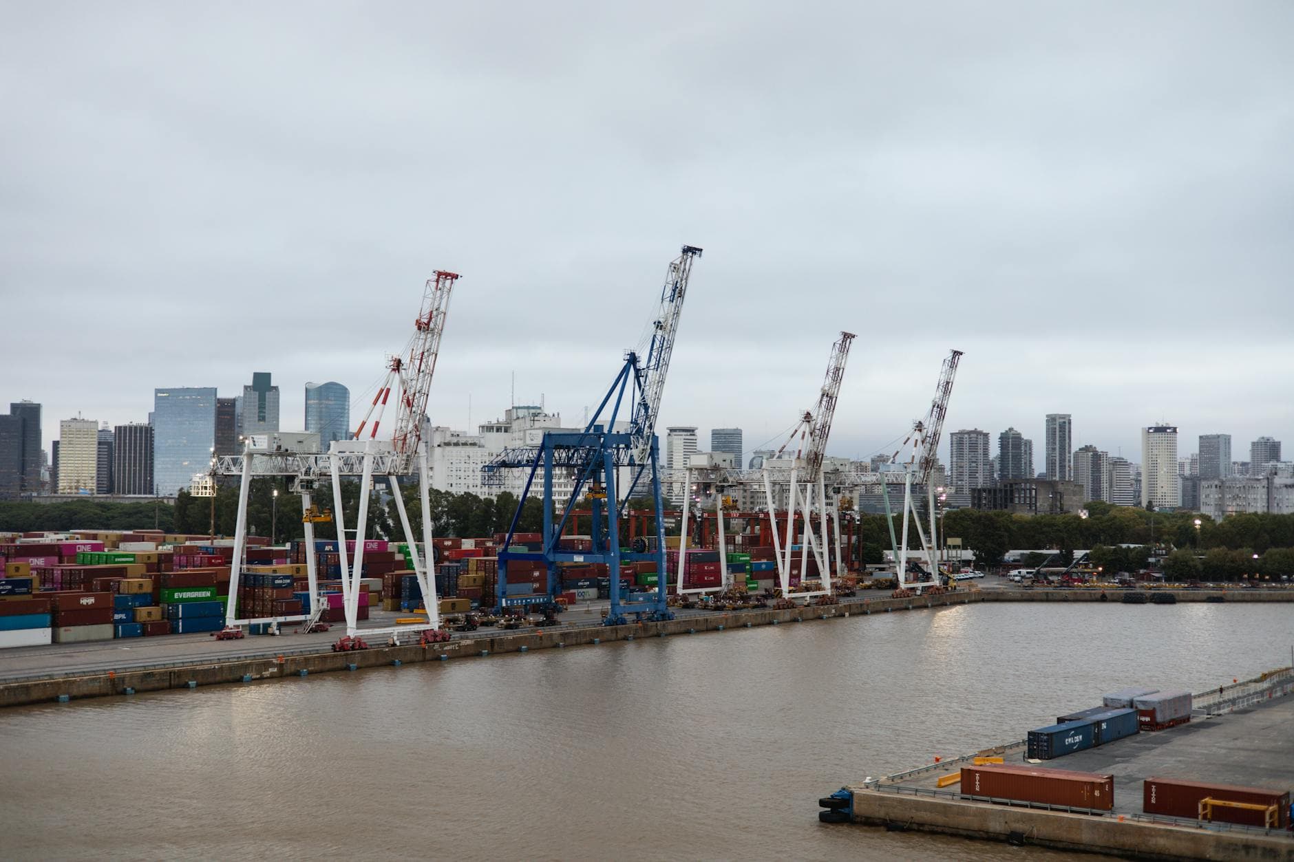 Contenedores de transporte y grúas en un puerto bullicioso con el perfil urbano de la ciudad de fondo.
