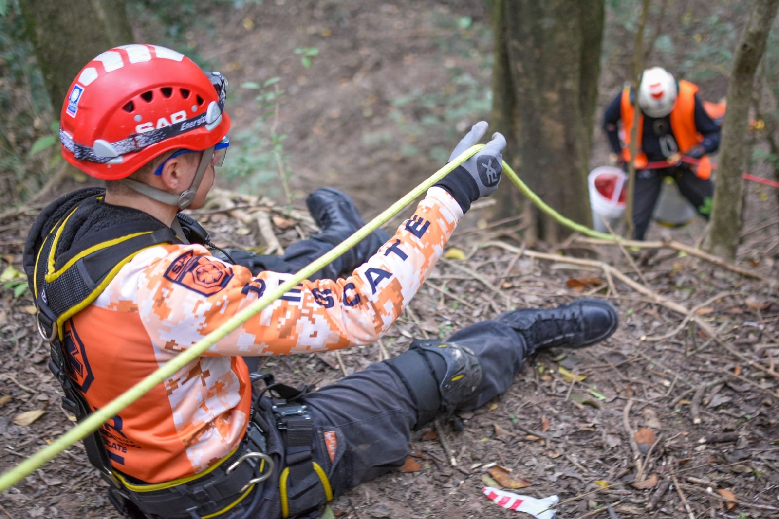 Equipo de búsqueda y rescate realizando una operación en una ladera forestal utilizando cuerdas de seguridad y cascos.
