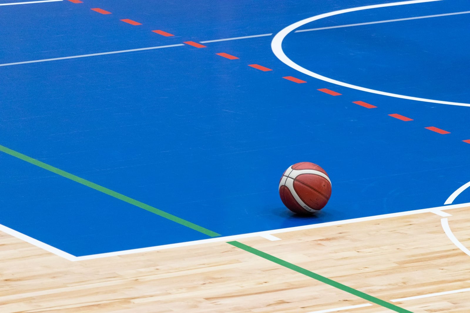 Un balón de baloncesto reposa sobre una vibrante cancha cubierta de color azul con suelo de madera y líneas coloridas.