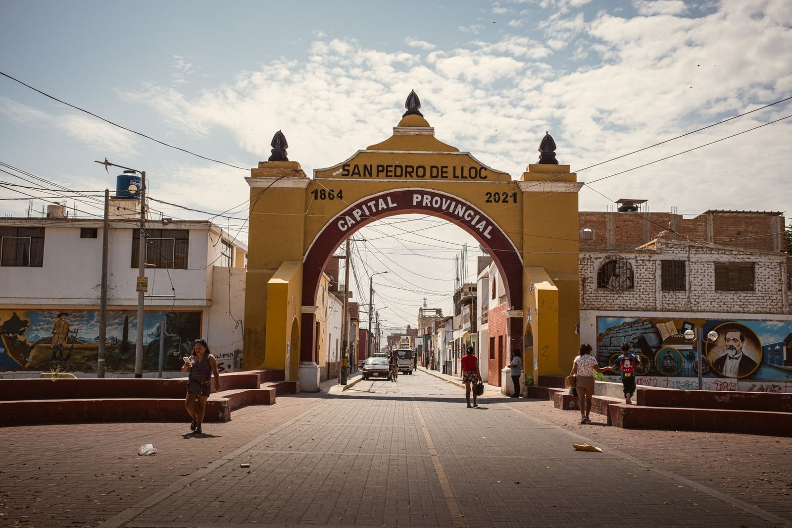 Vista a pie de calle del arco en San Pedro de Lloc, Perú, que muestra la vibrante vida urbana.