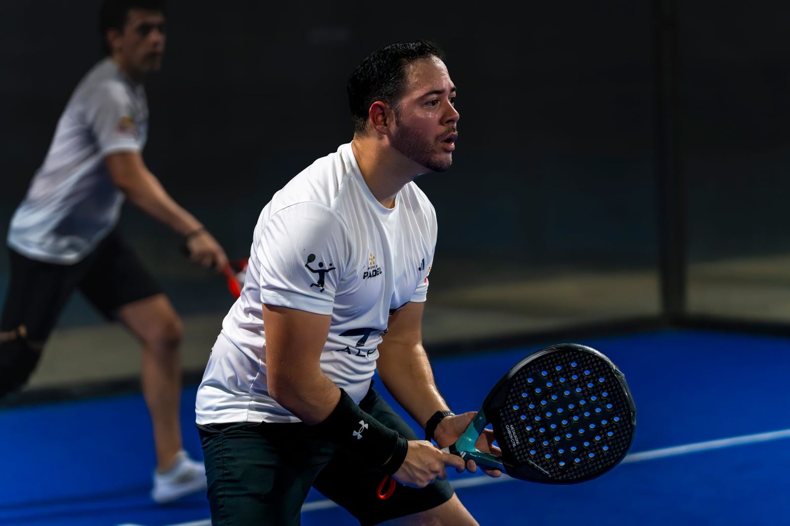 Dos hombres jugando un intenso partido de padel en una cancha cubierta azul brillante en Mérida, Yucatán, México.
