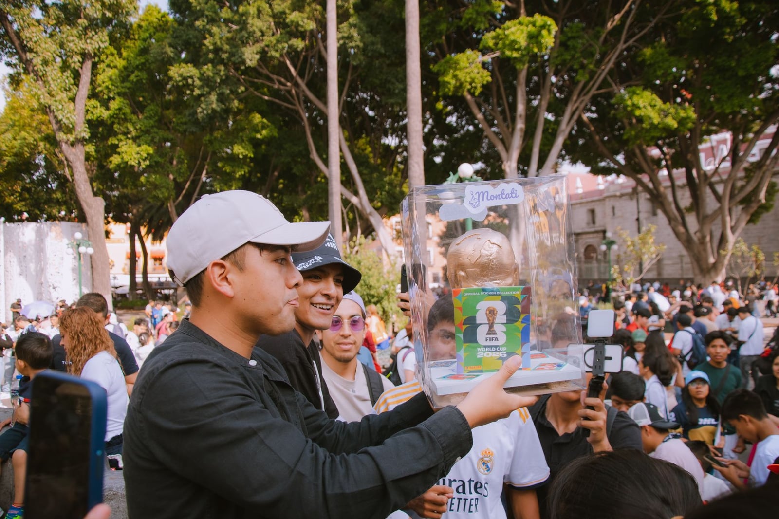 Grupo de personas celebrando con una réplica del trofeo de la Copa Mundial de la FIFA en un animado entorno al aire libre.