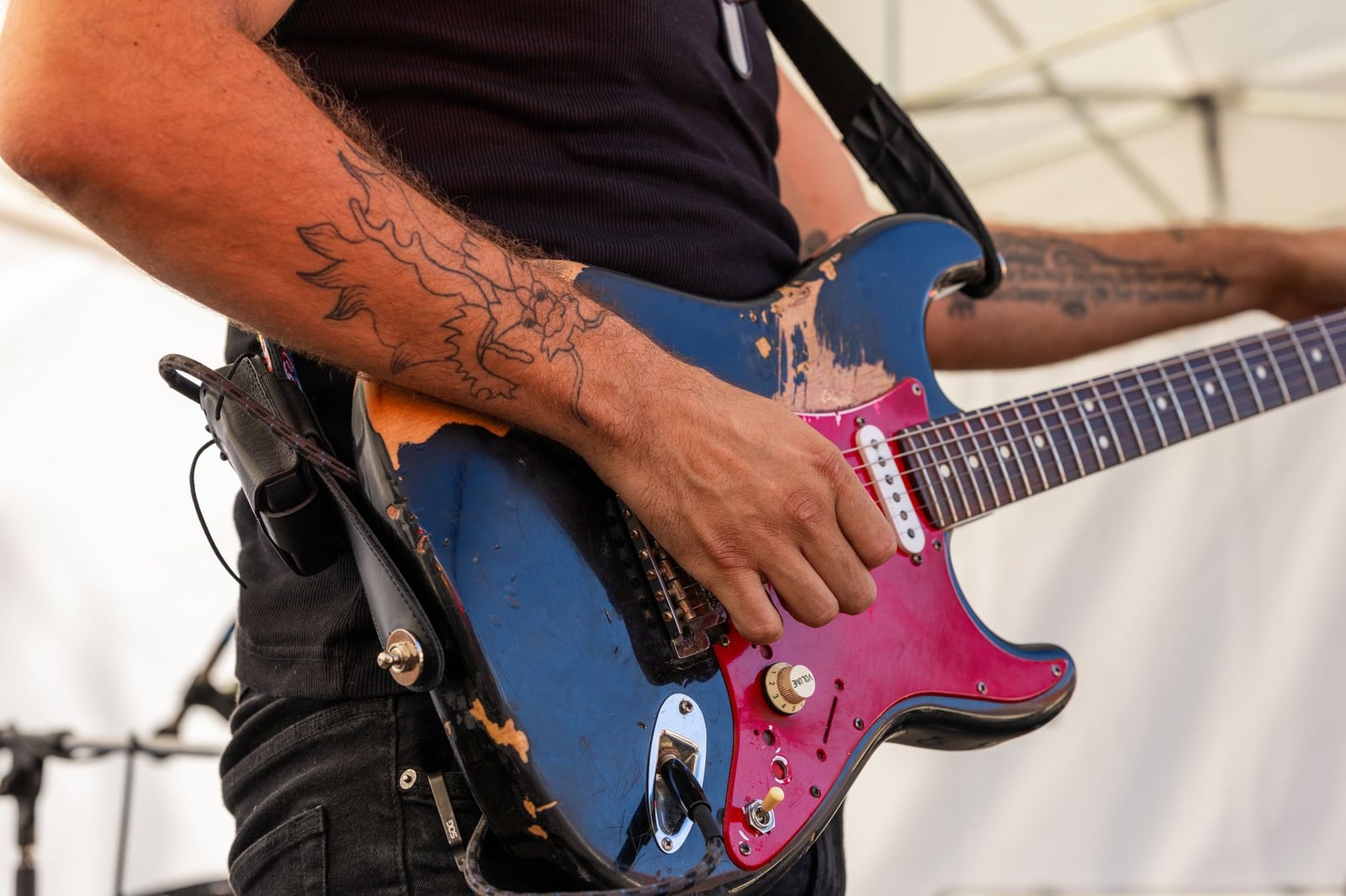 Primer plano de un guitarrista tocando una guitarra eléctrica en un concierto de rock al aire libre.