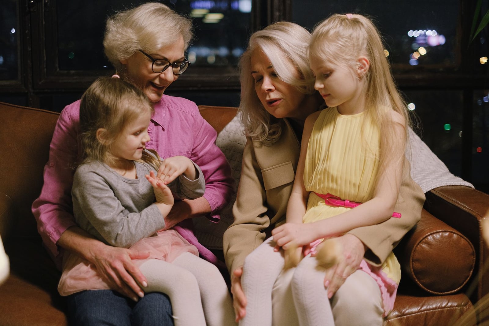 Un cálido momento familiar en interiores con dos abuelas y dos nietas sentadas juntas en un sofá.