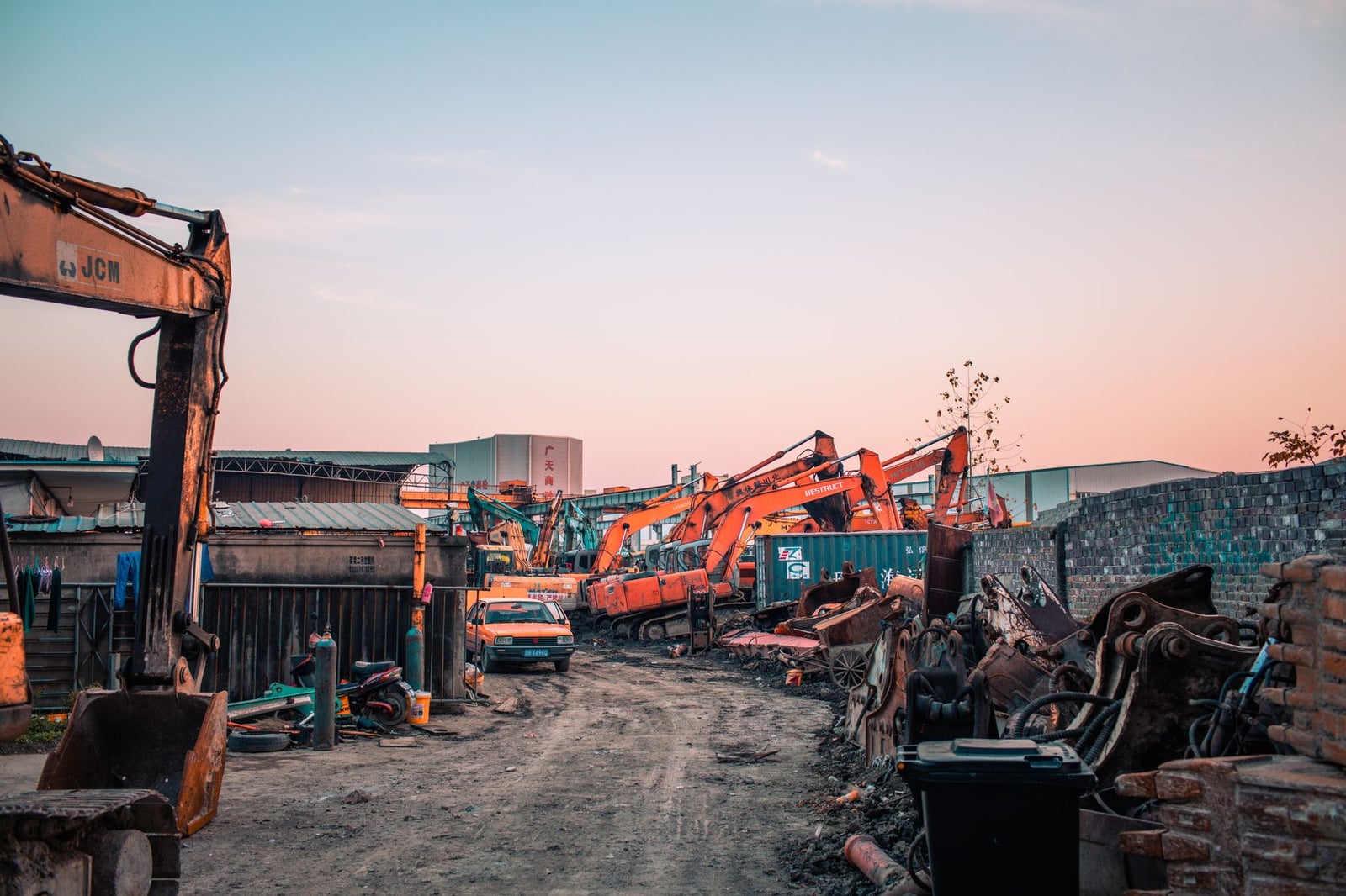 Un ocupado sitio de construcción con maquinaria industrial al atardecer, mostrando excavadoras y un cielo vibrante.