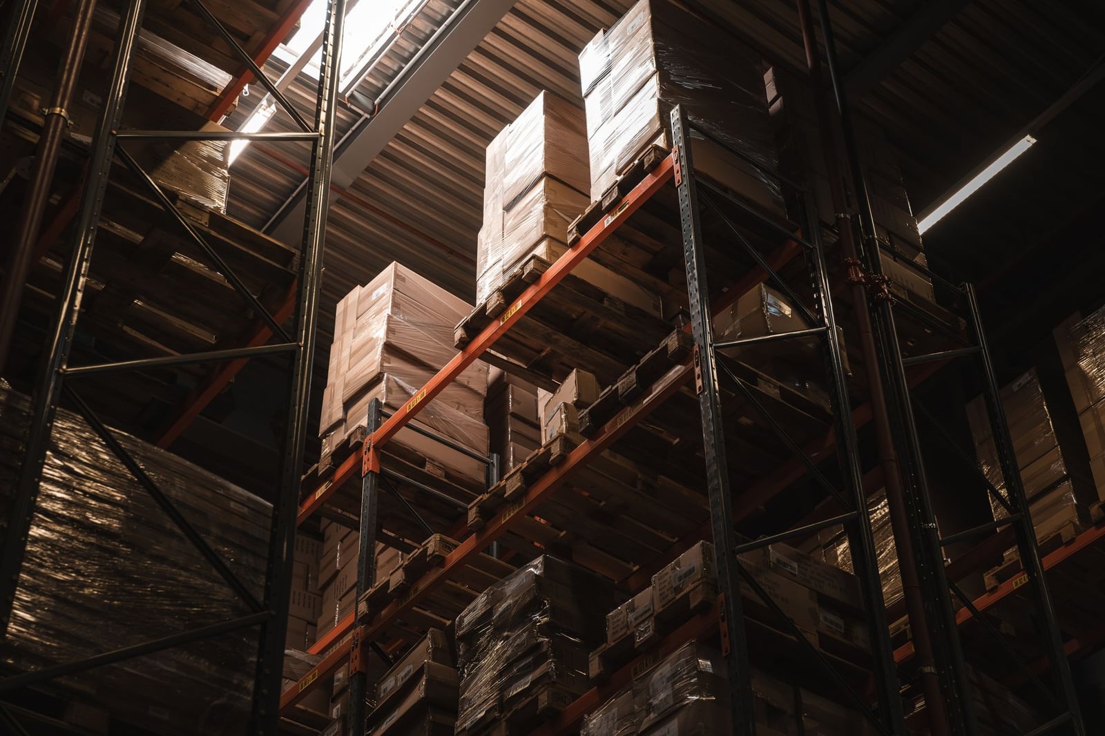 Vista interior de un almacén con cajas de cartón apiladas en estantes altos, mostrando almacenamiento y logística.