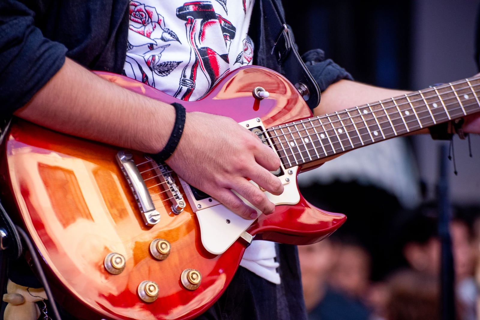 Primer plano vibrante de un guitarrista tocando una guitarra eléctrica roja en un evento al aire libre.