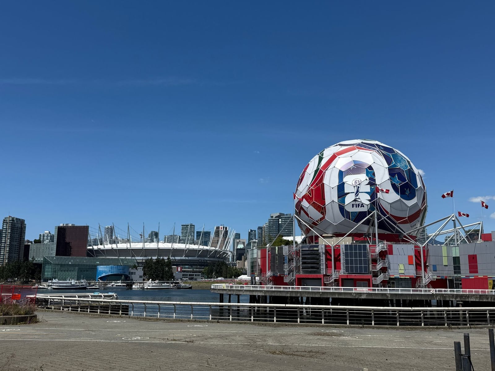 Vista del Science World de Vancouver, con la exhibición de la FIFA y el estadio BC Place bajo un cielo azul despejado.
