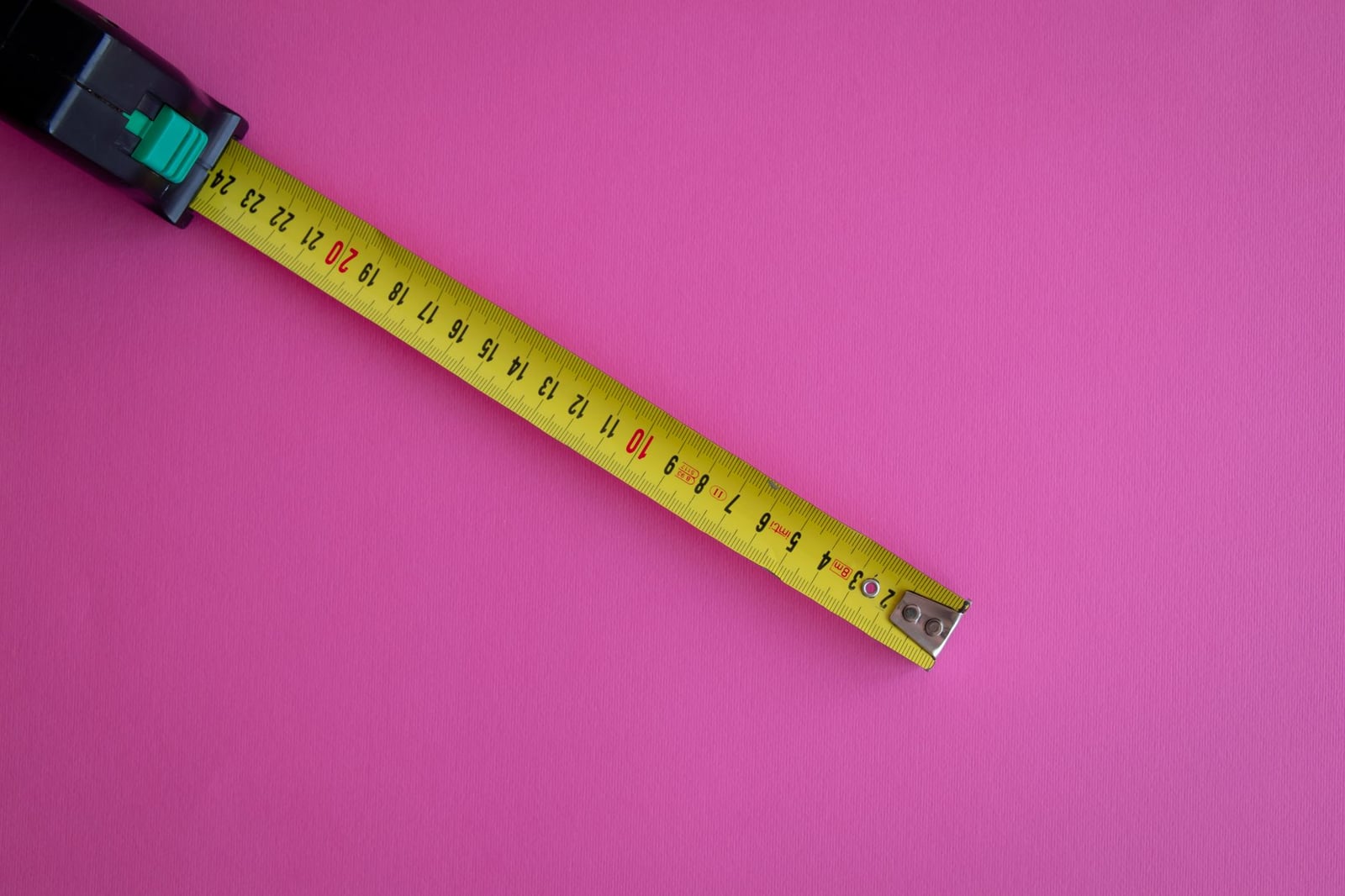 Una cinta métrica amarilla extendida sobre un vibrante fondo rosa, ofreciendo amplio espacio para texto.