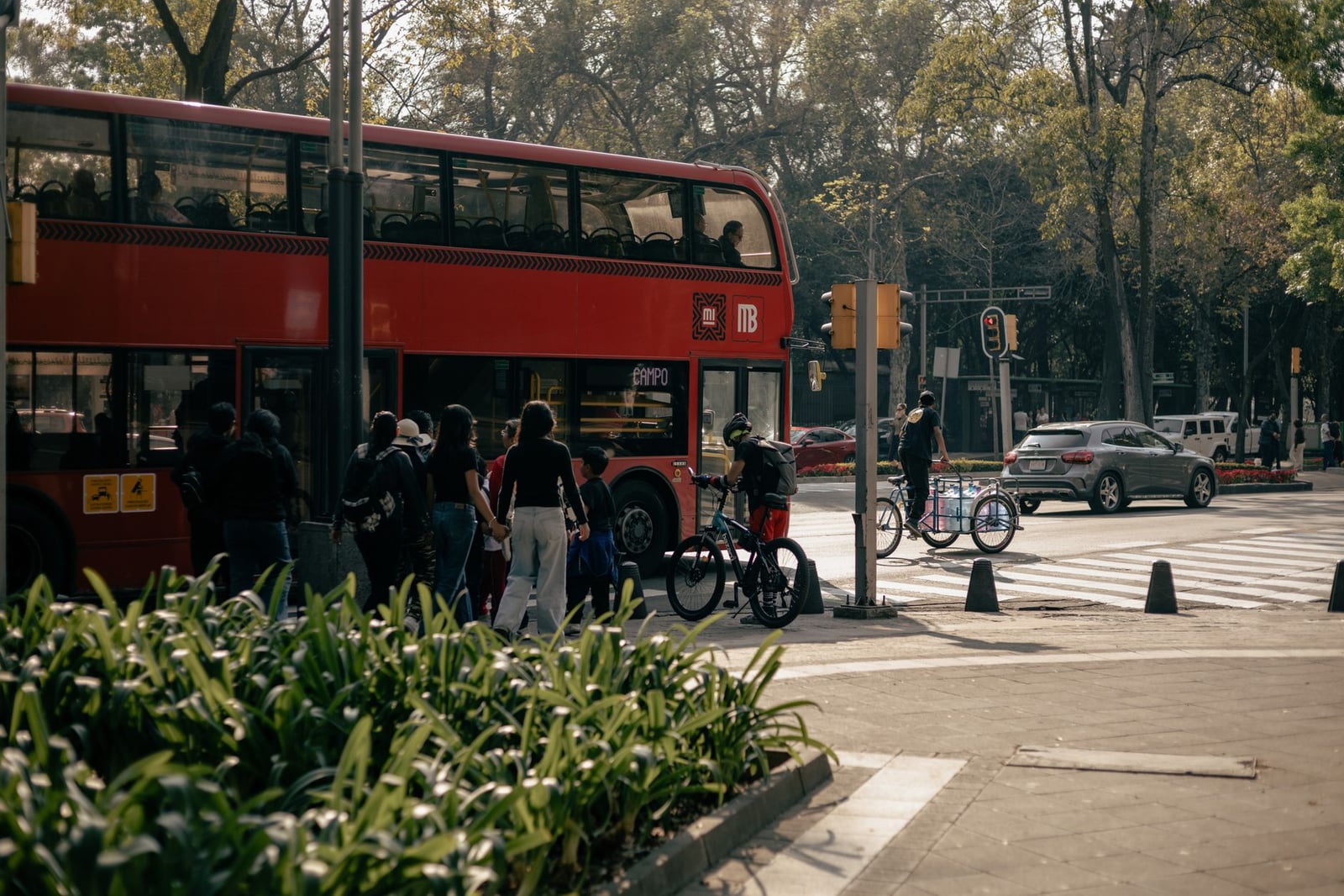Escena callejera concurrida en Ciudad de México con un autobús rojo brillante de dos pisos y ciclistas en un cruce de peatones.
