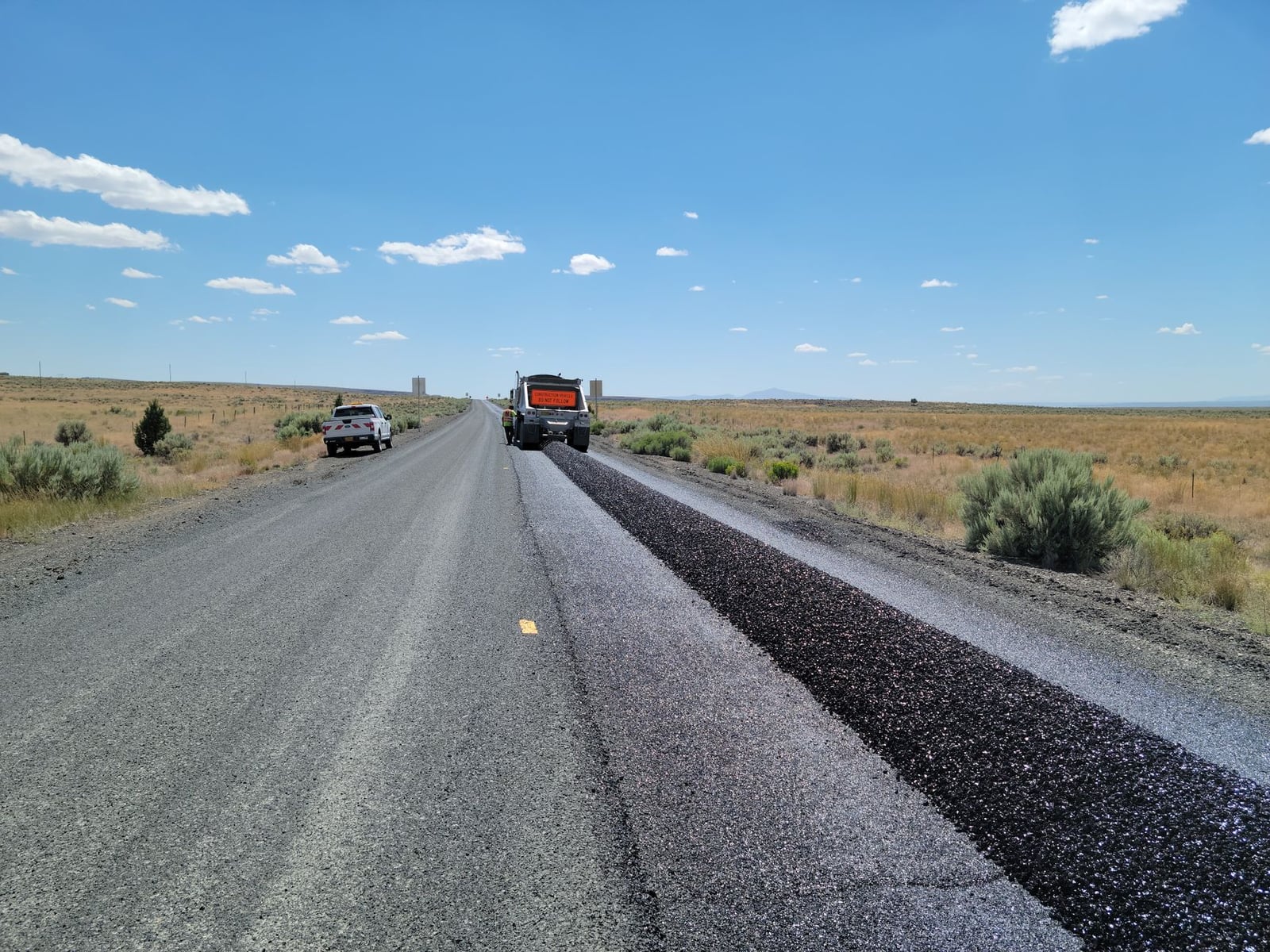 Equipo de construcción renovando una carretera rural bajo un cielo azul claro.