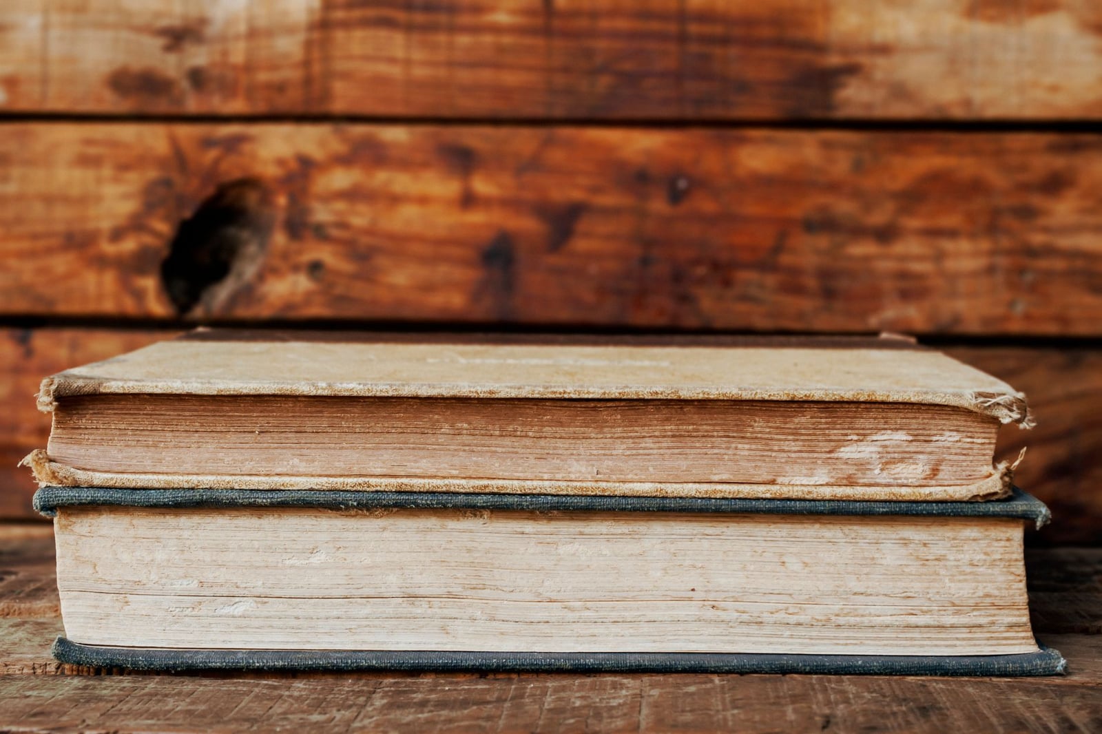 Acercamiento de dos libros vintage apilados contra un fondo de madera rústica, destacando la textura y la antigüedad.
