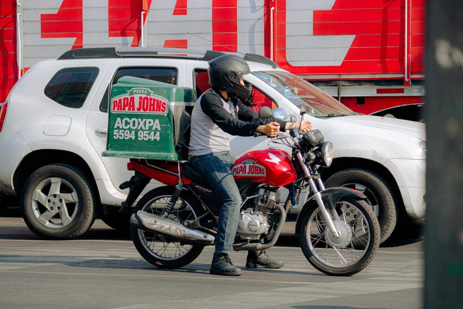 Repartidor de pizza en una motocicleta espera en una concurrida intersección de calles de la ciudad.