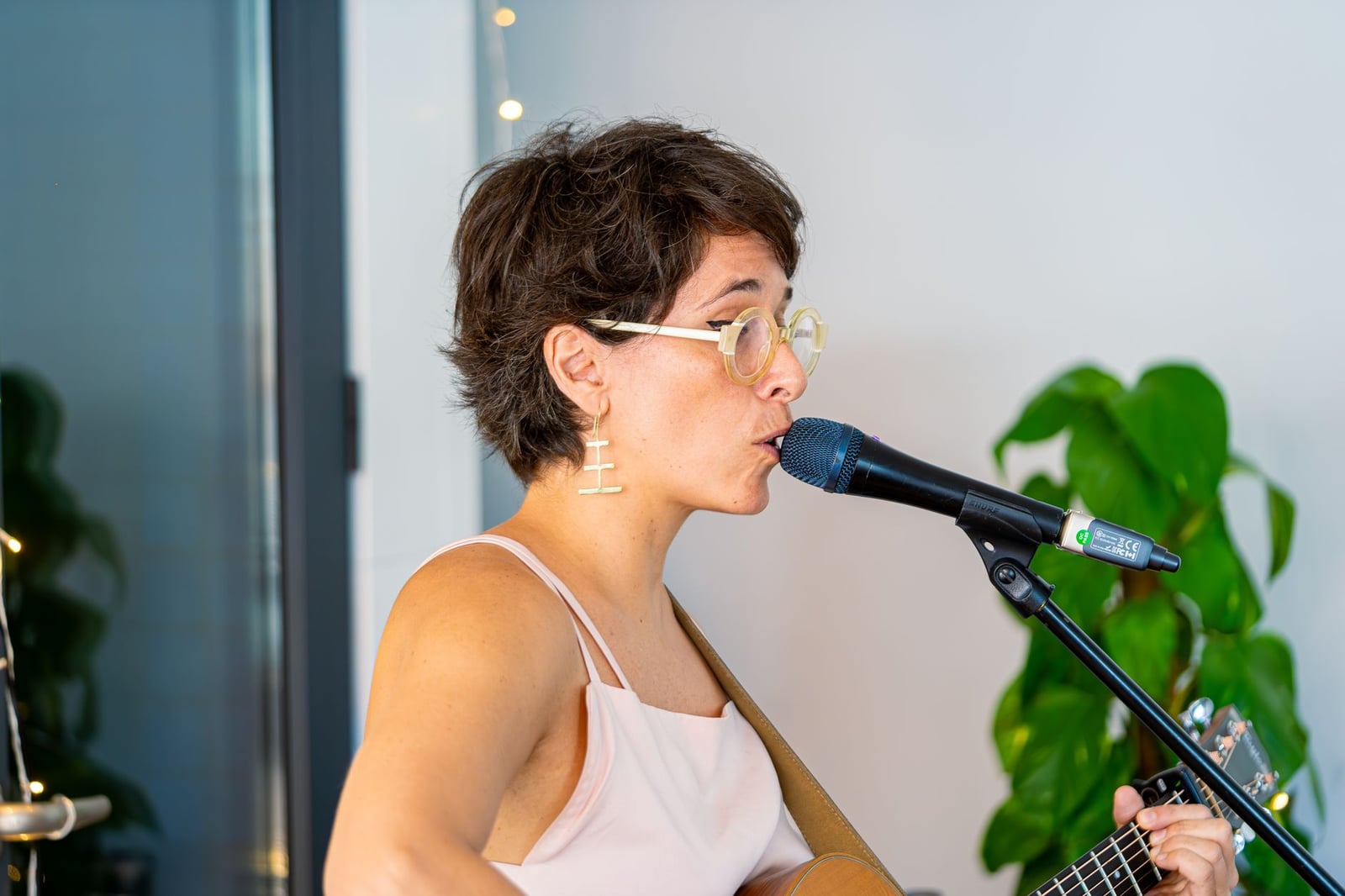 Una mujer canta en un micrófono mientras toca la guitarra en un interior, expresando su pasión musical.